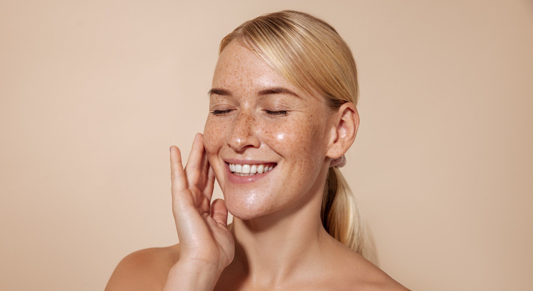 Woman smiling with freckles against a neutral background.